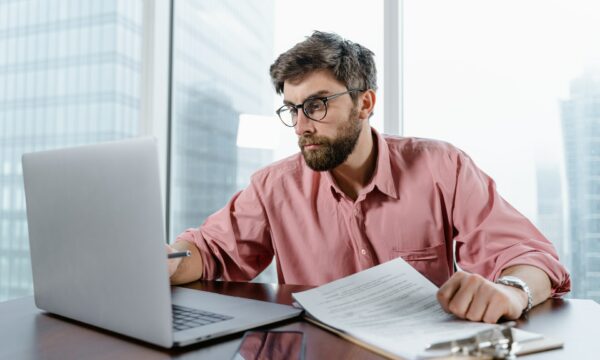 Man in Red Dress Shirt Wearing Black Framed Eyeglasses Using Macbook Air